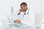 Side view of a concentrated male doctor using cellphone and laptop at medical office