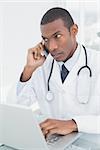 Concentrated male doctor using cellphone and laptop at medical office