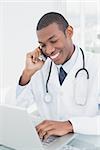 Smiling male doctor using cellphone and laptop at medical office