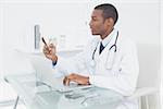 Side view of a male doctor text messaging while using laptop at medical office