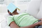 Relaxed young man with book over face lying on sofa in a bright house