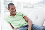 Smiling relaxed young Afro man sitting on sofa in a bright house