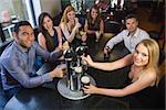 Young friends sitting together and pulling pints in a restaurant smiling at camera