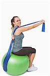Cheerful woman stretching her arms using a resistance band sitting on balance ball