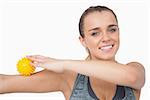 Cheerful young woman touching arm with massage ball on white screen