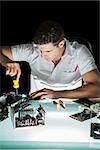 Handsome computer engineer working by night with screw driver at his lit desk