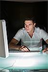 Handsome concentrating computer engineer working at night at his lit desk