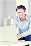 Cmiling casual man looking at camera using laptop in bright living room