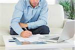 Close up of man writing on sheets paying bills in bright living room