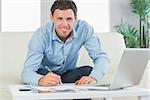 Smiling casual man writing on sheets paying bills in bright living room