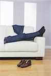 Close up of male legs in suit lying on couch in bright living room