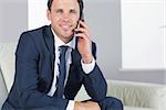 Smiling handsome businessman phoning and sitting on couch in bright living room