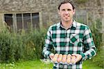 Young smiling man holding carton of eggs in his garden