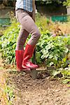 Woman working in the garden with a shovel wearing red rubber boots