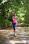 Lovely young woman jogging towards camera in a forest on sunny day