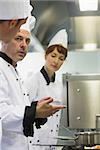 Male mature chef explaining something to a colleague while standing in front of the cooker