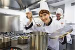 Young female chef tasting a soup and smiling at camera in kitchen