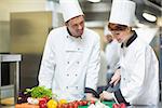 Female chef slicing vegetables with colleague in commercial kitchen
