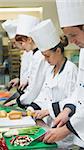 Chefs standing in a row cutting vegetables in a kitchen