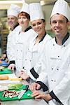 Four chefs standing in a row smiling at the camera in a kitchen