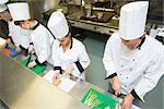 Four chefs preparing food at counter standing in a row in a kitchen