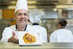 Experienced mature chef presenting a dish smiling at the camera