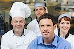 Young manager posing in a kitchen with chefs smiling at camera