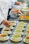 Bowls with soup being garnished with basil leaves on counter