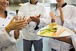 Young chefs applauding a salmon dish in commercial kitchen