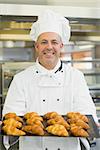 Mature baker presenting some croissants on a baking tray