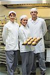 Young female baker presenting some rolls posing with her colleagues