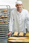 Young male baker standing in a kitchen in front of baguettes and rolls