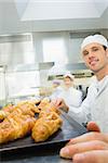 Young male baker standing in a bakery in front of a baking tray with croissants