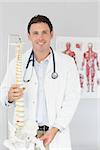 Handsome smiling doctor holding skeleton model in his office looking at camera