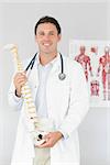 Handsome cheerful doctor holding skeleton model in bright office