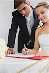 Young smiling bride signing wedding contract being watched by her husband