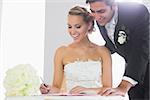 Happy young couple signing wedding register sitting at desk
