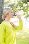 Fit calm blonde drinking from water bottle in a park on a sunny day