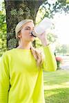 Fit calm blonde drinking from sports bottle in a park on a sunny day