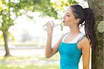 Active peaceful brunette drinking from a water bottle in a park on a sunny day