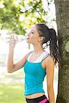 Active pretty brunette drinking from a water bottle in a park on a sunny day