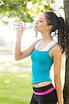 Active attractive brunette drinking from a water bottle in a park on a sunny day