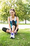 Active cheerful brunette tying her shoelaces in a park on a sunny day