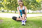 Active content brunette tying her shoelaces in a park on a sunny day