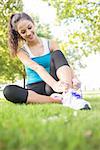 Happy active brunette tying her shoelaces in a park on a sunny day