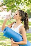 Active calm brunette holding exercise mat in a park on a sunny day