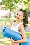 Active cheerful brunette holding exercise mat in a park on a sunny day