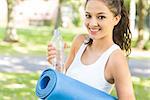 Active content brunette holding exercise mat in a park on a sunny day