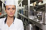 Young unsmiling chef standing arms crossed between shelves in professional kitchen