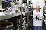 Young happy chef standing arms crossed between shelves in professional kitchen